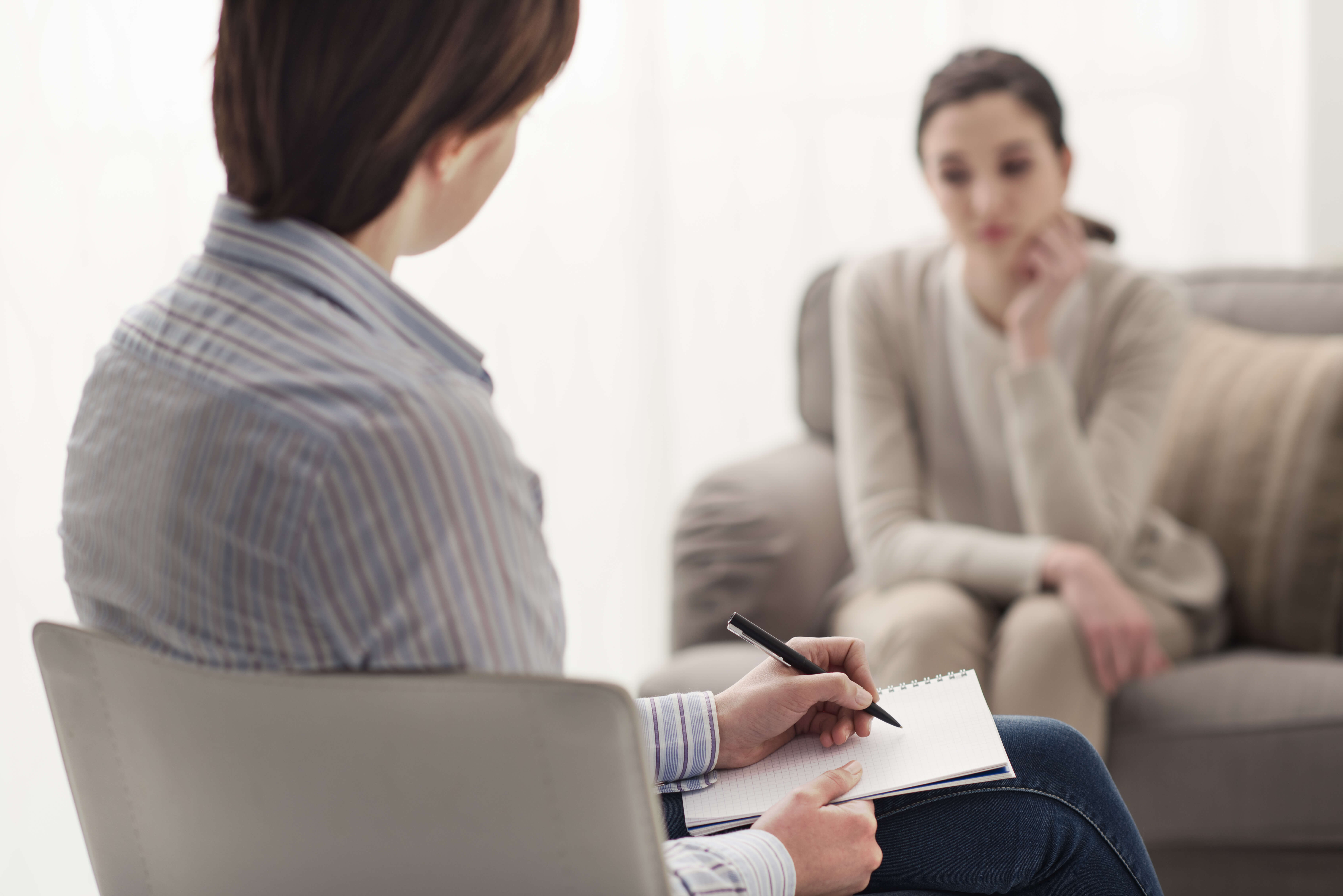 A woman sitting in front of another person holding a pen.